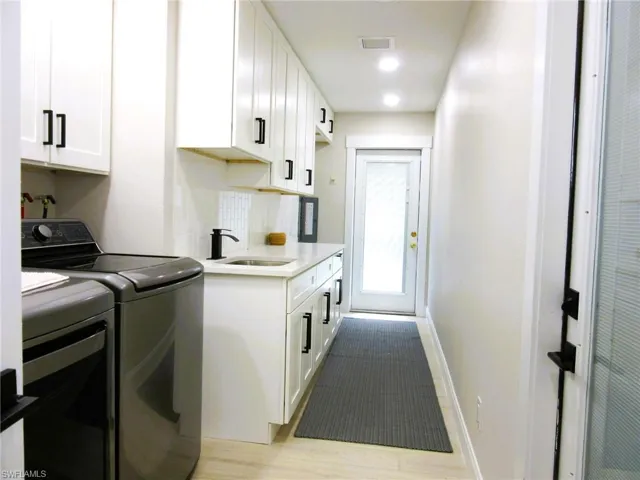 Kitchen featuring independent washer and dryer, white cabinetry, tasteful backsplash, sink, and light hardwood / wood-style floors