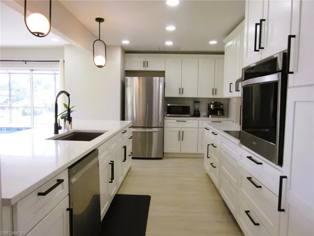 Kitchen featuring pendant lighting, white cabinetry, light hardwood / wood-style flooring, sink, and appliances with stainless steel finishes