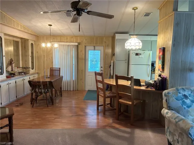 Kitchen with hardwood / wood-style floors, wood walls, white refrigerator, ceiling fan with notable chandelier, and hanging light fixtures