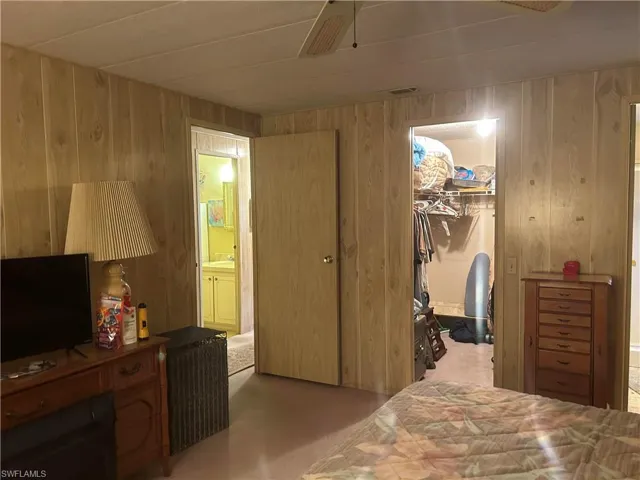Bedroom with ceiling fan, light carpet, wood walls, a closet, and ensuite bathroom