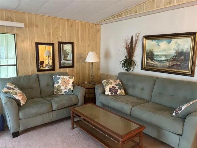Living room featuring carpet floors, wooden walls, and lofted ceiling