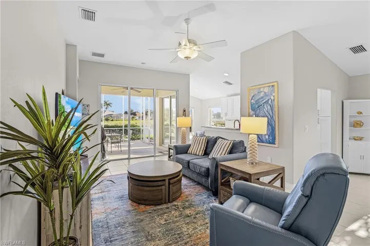 Living area featuring high ceilings, neutral wall tones, large-format tile flooring, a ceiling fan with integrated lighting, and sliding glass doors leading to a screened-in lanai