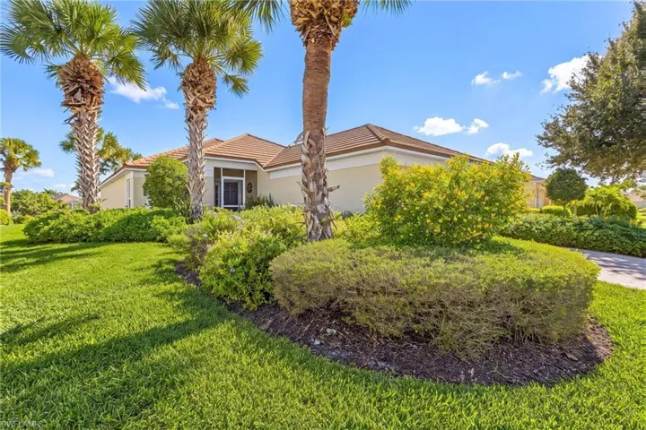 Single-story exterior featuring a tile roof, light-toned stucco facade, manicured lawn, established landscaping, and palm trees