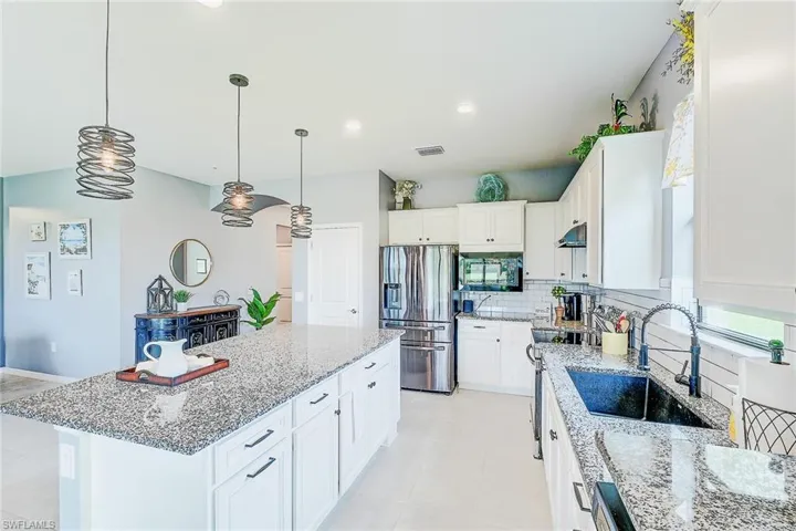 Kitchen with stainless steel fridge, pendant lighting, a kitchen island, sink, and white cabinetry