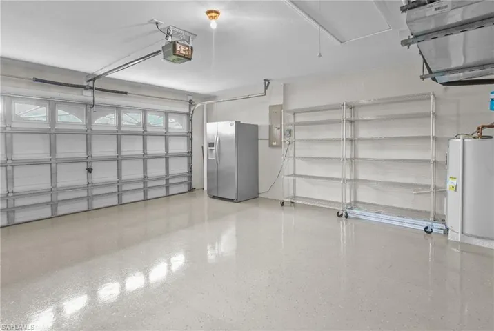 Garage featuring stainless steel fridge, water heater, electric panel, and a garage door opener
