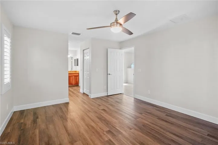 Unfurnished bedroom featuring wood finished floors, ensuite bathroom, and a ceiling fan