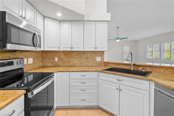 Kitchen with stainless steel appliances, white cabinets, light tile patterned flooring, light stone counters, and decorative backsplash