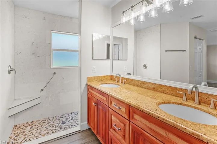 Bathroom featuring double vanity, walk in shower, and wood finished floors