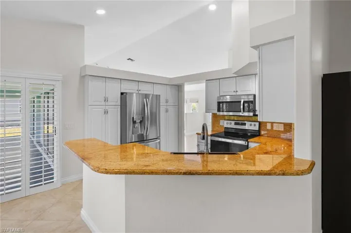 Kitchen with stainless steel appliances, light stone counters, a peninsula, decorative backsplash, and recessed lighting