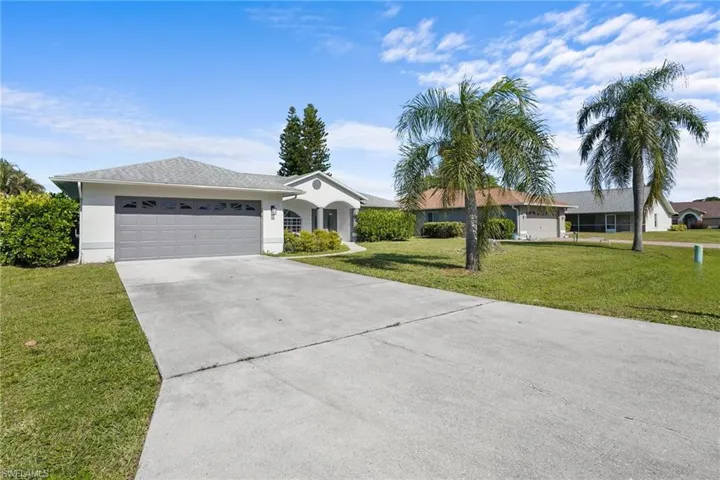 Ranch-style house featuring an attached garage, concrete driveway, a front lawn, and stucco siding