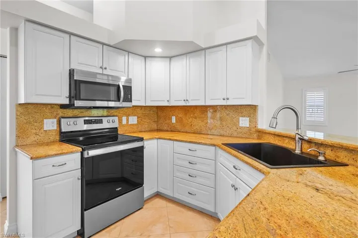 Kitchen with appliances with stainless steel finishes, white cabinets, light tile patterned flooring, tasteful backsplash, and light stone countertops