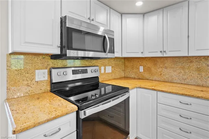 Kitchen with appliances with stainless steel finishes, white cabinetry, and light stone counters
