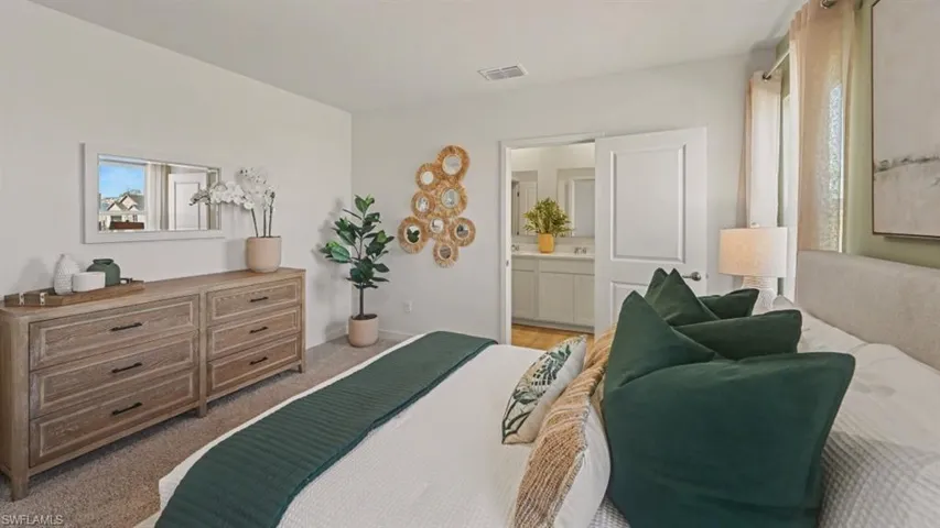 Carpeted bedroom featuring a light-colored wall, a white interior door, and an open doorway revealing a bathroom with a double vanity