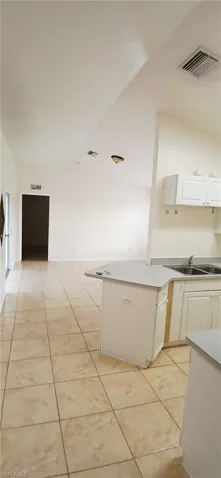 Kitchen featuring light tile patterned flooring, white cabinets, light countertops, and vaulted ceiling