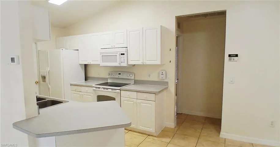 Kitchen featuring white appliances, light countertops, lofted ceiling, light tile patterned floors, and white cabinets