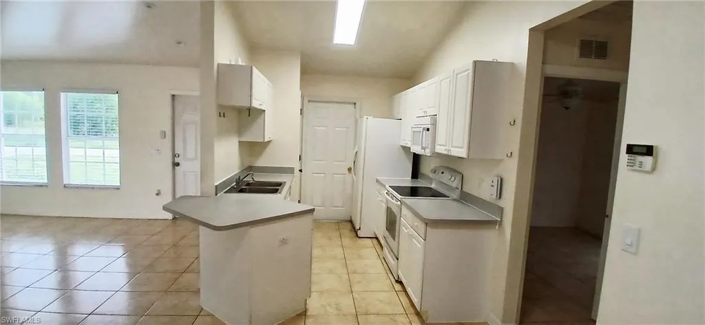 Kitchen with white cabinetry, white appliances, a peninsula, light tile patterned flooring, and light countertops