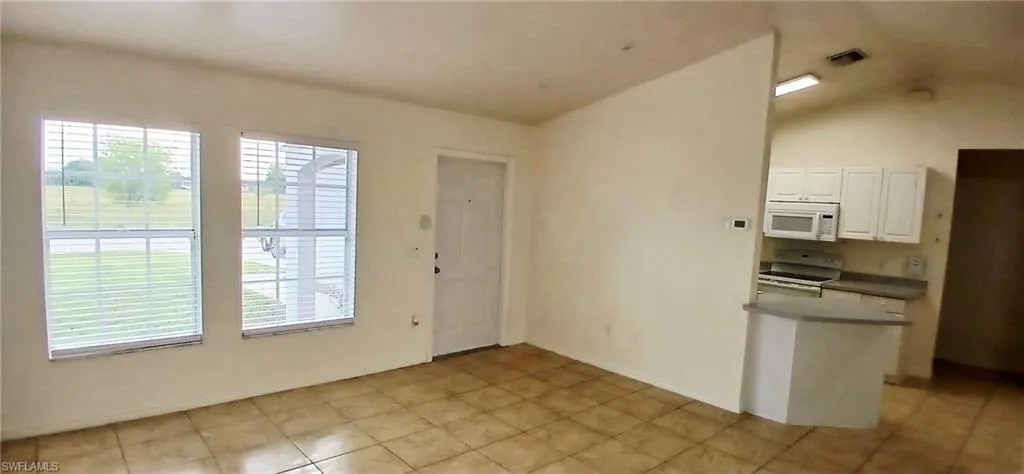 Kitchen featuring white cabinets, white appliances, vaulted ceiling, and light tile patterned floors