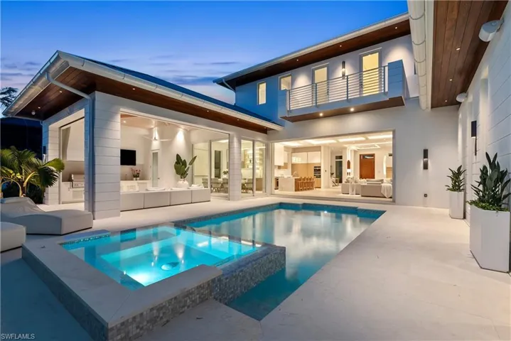 Back house at dusk featuring a swimming pool with hot tub, an outdoor living space, a balcony, and a patio area