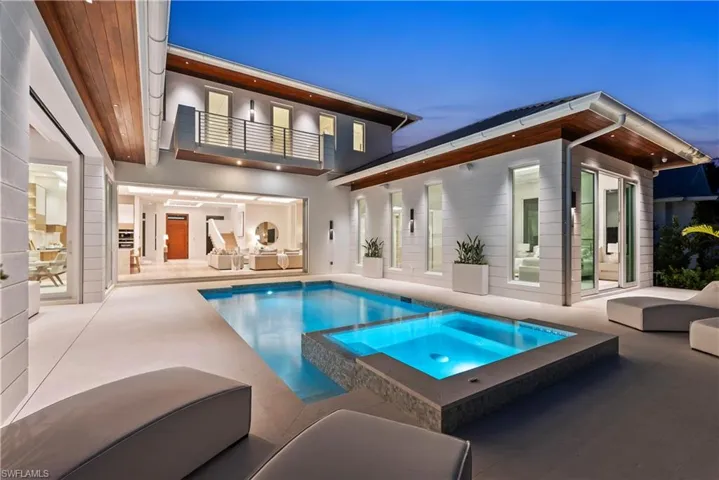 Back house at dusk featuring a swimming pool with hot tub, a patio, and a balcony
