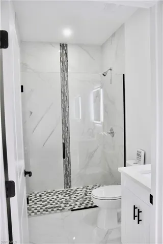 Bathroom with a marble finish shower, marble finish floor, toilet, and vanity