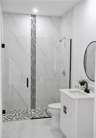 Bathroom with toilet, marble finish floor, a marble finish shower, and vanity