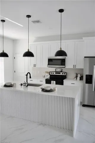 Kitchen with a sink, visible vents, light countertops, appliances with stainless steel finishes, and an island with sink