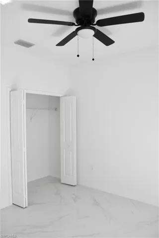 Unfurnished bedroom featuring a closet, marble finish floor, visible vents, and ceiling fan