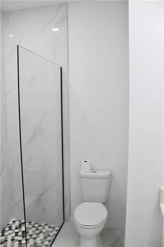 Bathroom with a marble finish shower, marble finish floor, baseboards, and toilet