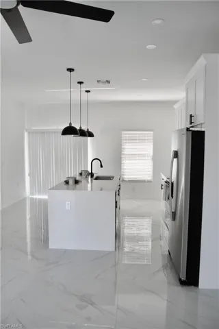 Kitchen featuring stainless steel fridge with ice dispenser, marble finish floor, a kitchen island with sink, white cabinetry, and a sink