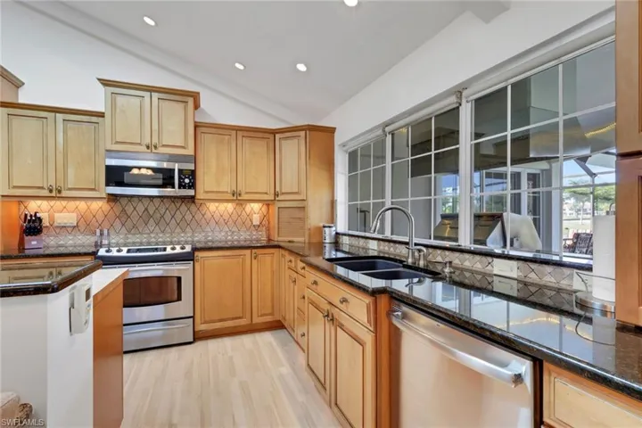 Kitchen featuring vaulted ceiling, stainless steel appliances, decorative backsplash, dark stone counters, and light wood-style floors