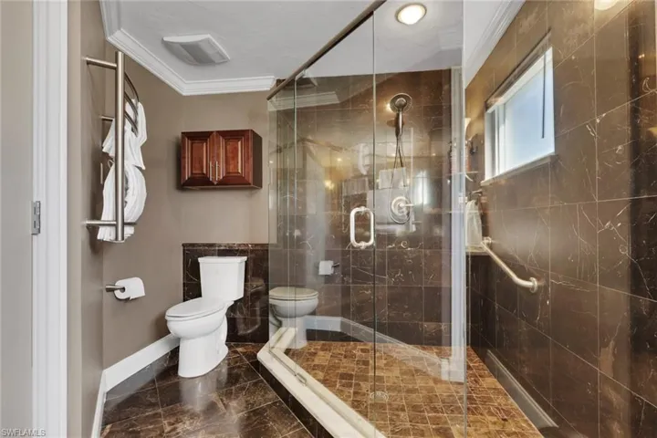 Bathroom featuring ornamental molding, a stall shower, and dark marble finish flooring
