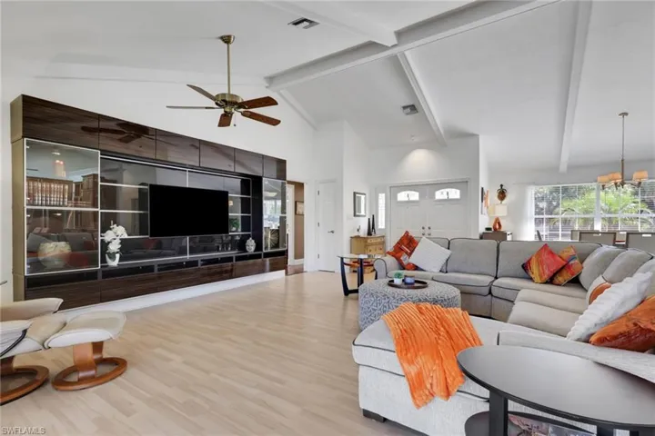 Living room featuring high vaulted ceiling, beam ceiling, wood finished floors, a chandelier, and a ceiling fan