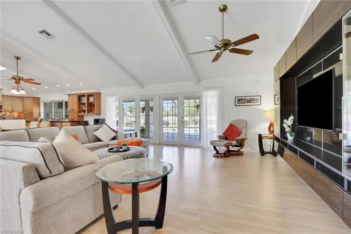 Living area featuring a ceiling fan, beamed ceiling, light wood-style floors, french doors, and high vaulted ceiling