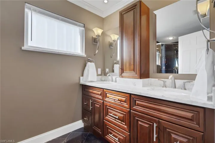 Full bathroom with ornamental molding, double vanity, a shower stall, and dark marble finish floors