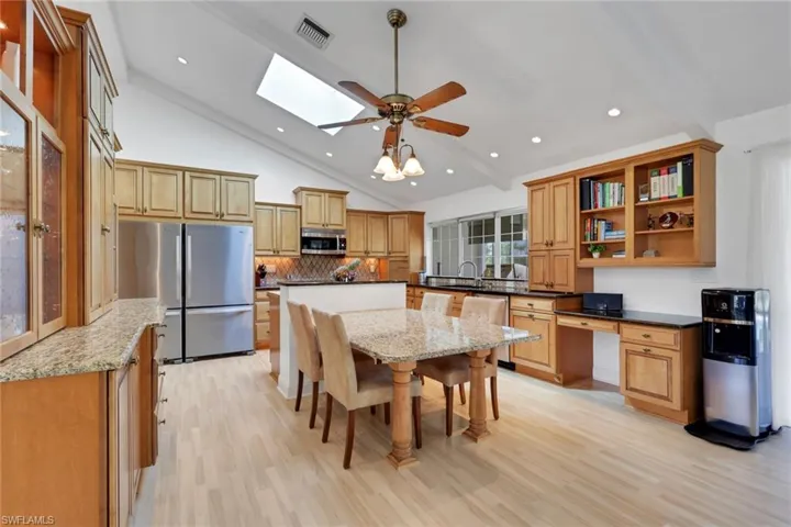 Kitchen with tasteful backsplash, stainless steel appliances, open shelves, dark stone countertops, and a skylight