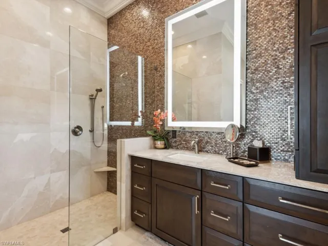 Bathroom featuring a shower with shower door, crown molding, tasteful backsplash, and vanity
