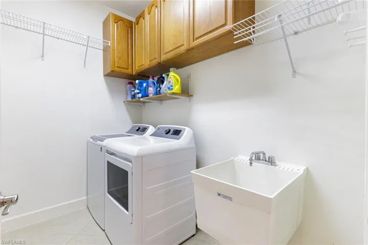 Laundry area with light tile patterned floors, washer and dryer, and cabinet space