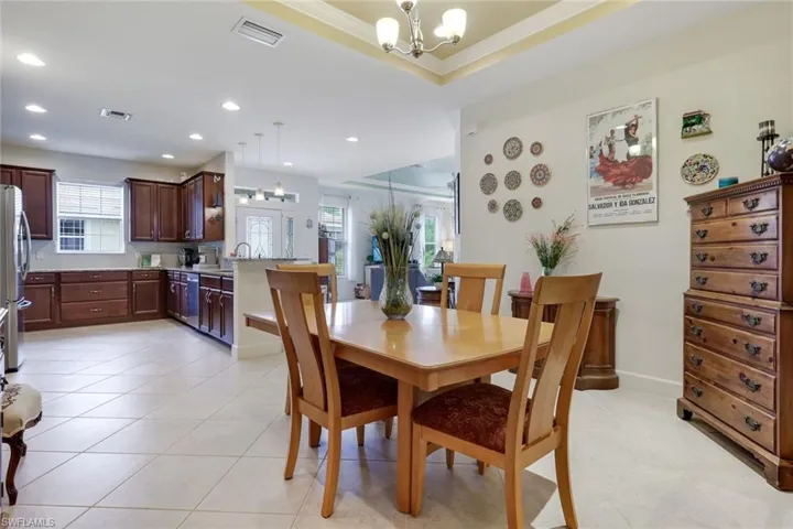 Dining space featuring healthy amount of natural light, a chandelier, light tile patterned floors, a raised ceiling, and recessed lighting