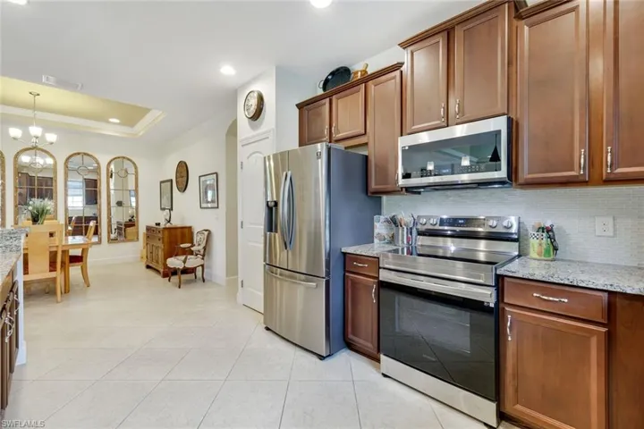 Kitchen featuring appliances with stainless steel finishes, light stone countertops, a raised ceiling, backsplash, and brown cabinetry
