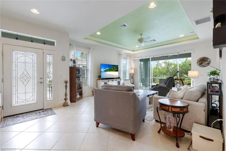Living area featuring a tray ceiling, light tile patterned floors, recessed lighting, and ceiling fan