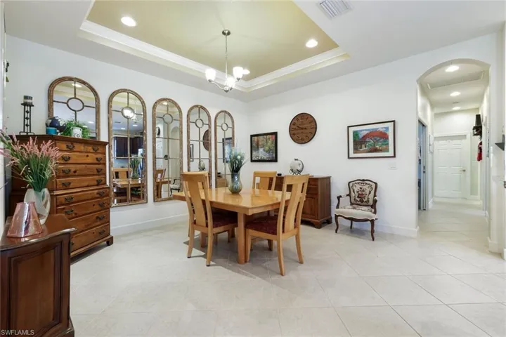 Dining space featuring a tray ceiling, recessed lighting, arched walkways, crown molding, and light tile patterned floors