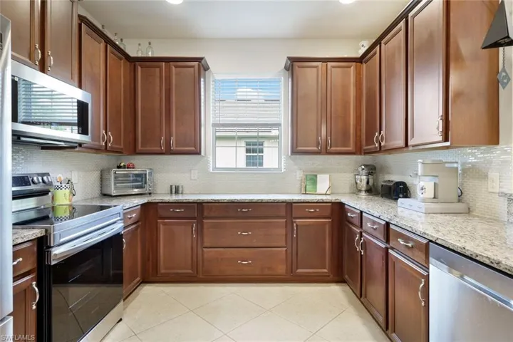 Kitchen featuring backsplash, stainless steel appliances, light stone countertops, light tile patterned flooring, and recessed lighting