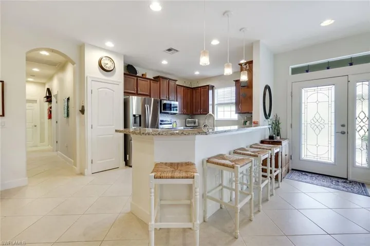 Kitchen with a breakfast bar, arched walkways, light tile patterned flooring, pendant lighting, and light stone counters