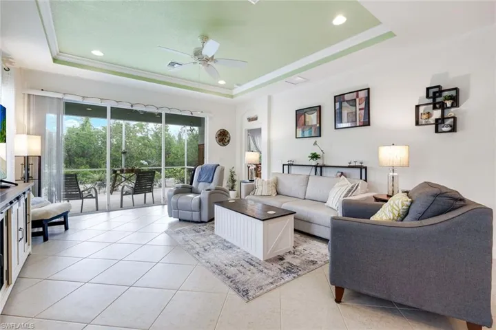 Living area with light tile patterned floors, a tray ceiling, a ceiling fan, recessed lighting, and ornamental molding