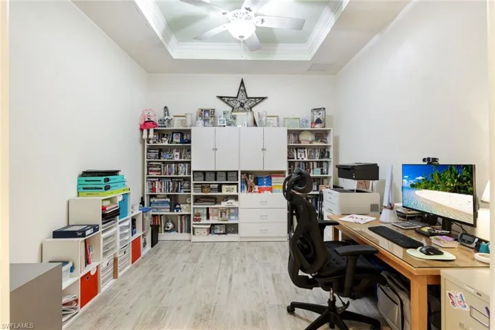 Office space with a ceiling fan, light wood-type flooring, a tray ceiling, and crown molding