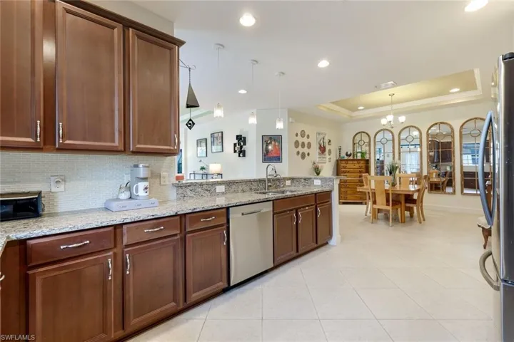 Kitchen featuring light stone countertops, a tray ceiling, decorative light fixtures, stainless steel appliances, and a chandelier