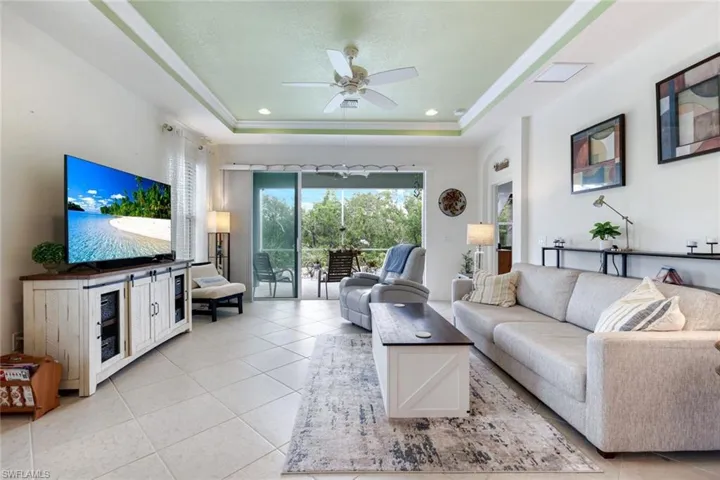 Living room with light tile patterned floors, ceiling fan, a tray ceiling, and recessed lighting