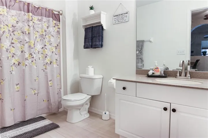 Full bath featuring toilet, vanity, curtained shower, and baseboards