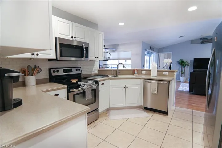 Kitchen with appliances with stainless steel finishes, a peninsula, a sink, decorative backsplash, and lofted ceiling