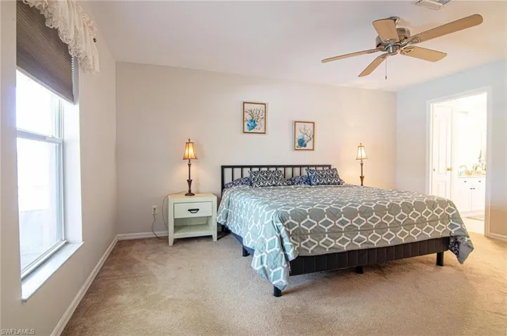 Bedroom with light carpet, multiple windows, baseboards, and ensuite bath